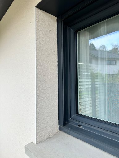 Coin d'un mur près d'une fenêtre avec des volets et un rebord de fenêtre.